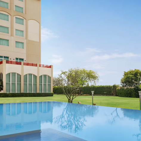 Ein glitzernder Pool spiegelt den blauen Himmel wider, umgeben von gepflegten Rasenflächen und modernen Gebäuden.