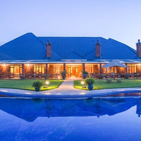 Ein elegantes Haus mit einem großen, blauen Pool und einer gepflegten Rasenfläche, umgeben von sanften Abendlichtern.