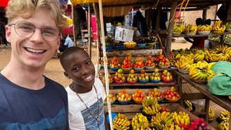 Zwei lächelnde Jungen stehen vor einem bunten Obststand, umgeben von einer Vielzahl frischer Früchte und Gemüse.