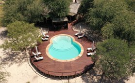 Ein runder Pool mit sanften Stufen ist von einer Holzterrasse und Liegen umgeben, umgeben von Bäumen in einer ruhigen Umgebung.