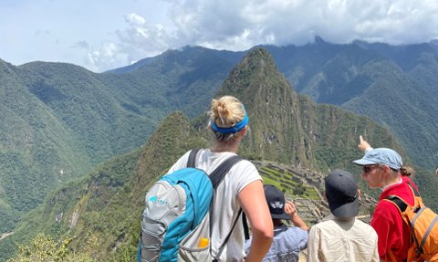 Eine Gruppe von Menschen steht auf einem Aussichtspunkt und bewundert die Ruinen von Machu Picchu inmitten der Berge.