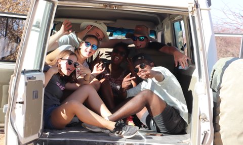 Eine Reisegruppe sitzt beisammen im offenen Kofferraum eines Jeeps - Namibia Rundreise mit Kindern