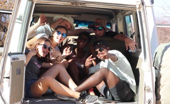 Eine Reisegruppe sitzt beisammen im offenen Kofferraum eines Jeeps - Namibia Rundreise mit Kindern