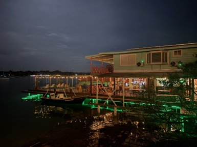 Ein gemütliches Restaurant am Wasser, beleuchtet von sanften Lichtern, mit Tischen und Stühlen auf der Terrasse.