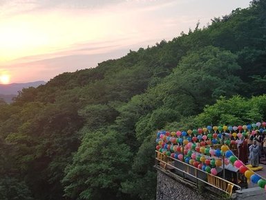 Eine Gruppe von Menschen steht auf einer Terrasse, umgeben von bunten Luftballons, während die Sonne hinter den Bergen untergeht.