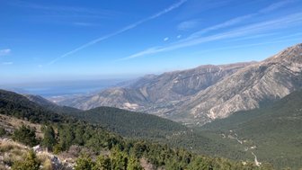 Ein atemberaubender Blick auf die Berge und das grüne Tal, das sich bis zum blauen Meer erstreckt, unter einem klaren Himmel.