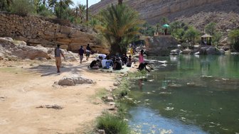 Menschen sitzen am Rand des Wassers im Wadi Shab – Oman Familienreise