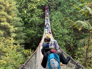 Eine Gruppe von Menschen überquert eine Hängebrücke, umgeben von üppigem, grünem Wald in Lynn Canyon.