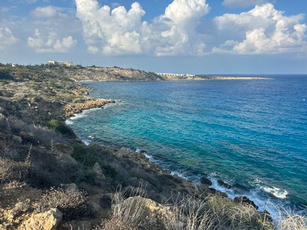 Eine malerische Küstenlandschaft mit klarem, blauem Wasser und sanften Wellen, umgeben von felsigen Ufern und bewachsenen Hügeln.