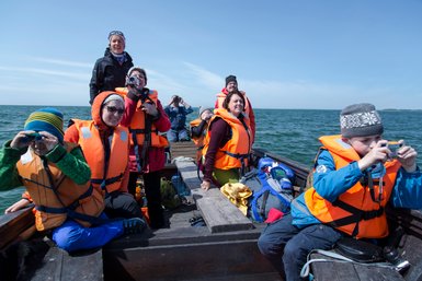 Eine Gruppe von Menschen in orangefarbenen Schwimmwesten genießt eine Bootstour auf dem Wasser, voller Freude und Neugier.