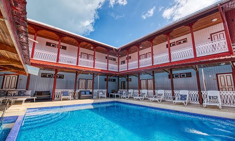 Ein einladender Pool umgeben von einem charmanten Hotel mit Holzveranda und blauen Himmel im Hintergrund.