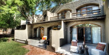 Eine moderne Lodge mit großen Fenstern und einem einladenden Außenbereich, umgeben von üppigem Grün und Bäumen.