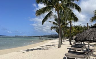 Ein ruhiger Strand mit feinem Sand, umgeben von Palmen und Liegen, die zum Entspannen einladen.