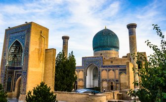 Die beeindruckende Architektur von Samarkand zeigt eine große Kuppel und kunstvoll verzierte Wände unter einem blauen Himmel.