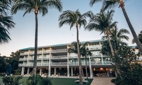 Eine moderne Hotelanlage umgeben von üppigen Palmen, die im sanften Abendlicht erstrahlen und einladend wirkt.