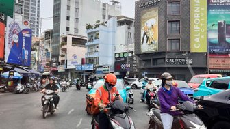 Zwei Motorradfahrer in der Stadt Saigon, umgeben von einem geschäftigen Verkehr und modernen Gebäuden im Hintergrund.