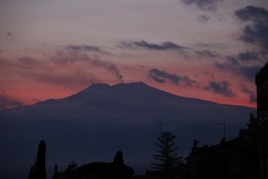Der Ätna erhebt sich majestätisch im Abendlicht, umgeben von sanften Wolken und einem farbenfrohen Himmel.