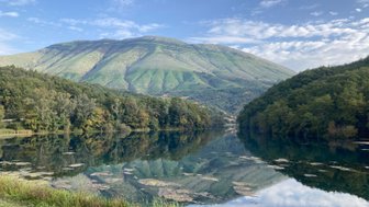 Ein ruhiger See spiegelt die sanften Hügel und den klaren Himmel wider, umgeben von üppigem Grün und sanften Wellen.