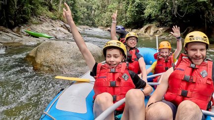 Familie im Schlauchboot lächelt in die Kamera, während sie den Fluss hinunterfährt – Malaysia & Borneo Familienreise