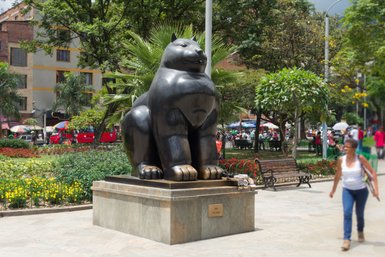 Eine große, glänzende Statue eines sitzenden Tieres steht in einem lebhaften Park voller Blumen und Bäume.