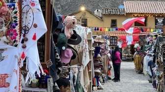 Bunte Stände mit traditioneller Kleidung und Handwerkskunst säumen die gepflasterte Straße in Ollantaytambo, umgeben von Bergen.