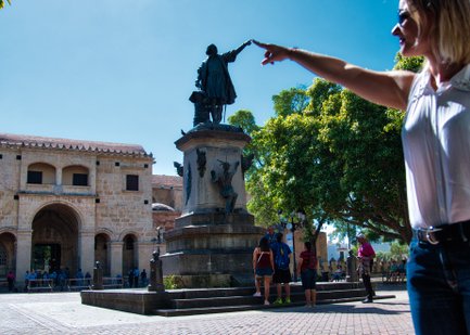 Eine Frau zeigt auf die Statue von Christoph Kolumbus im Parque Colón, umgeben von Besuchern und historischen Gebäuden.