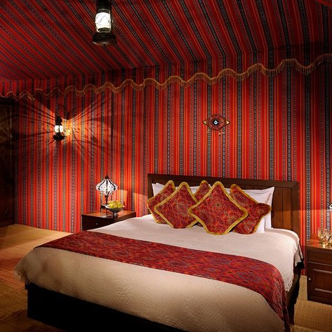 Ein gemütliches Schlafzimmer mit einem großen Bett, umgeben von rot gestreiften Wänden und bunten Kissen auf der Bettdecke.