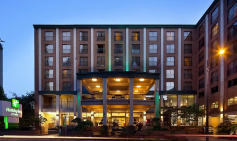 Das Holiday Inn & Suites in Vancouver zeigt eine moderne Fassade mit beleuchtetem Eingangsbereich und grünen Akzenten.