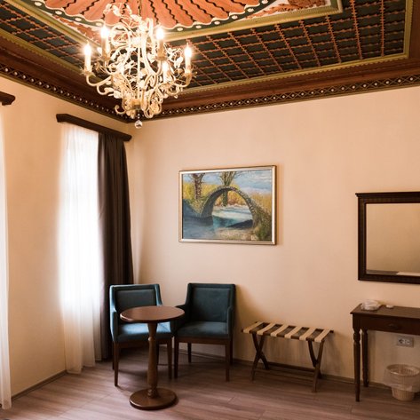 Ein elegantes Hotelzimmer mit einem Kronleuchter, zwei blauen Stühlen und einem kleinen Tisch, umgeben von hellen Vorhängen.