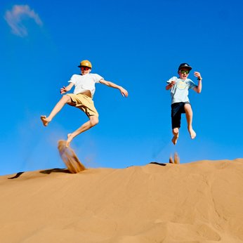 Kinder genießen die Freiheit und springen voller Freude auf den weiten Sanddünen der Wüste – Marokko Reise mit Kindern