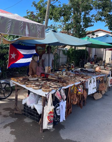 Ein belebter Marktstand in Vinales, Kuba, mit handgefertigten Holzartikeln und einer kubanischen Flagge im Hintergrund.