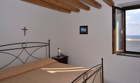 Ein gemütliches Schlafzimmer mit einem großen Fenster, das einen Blick auf das Meer und eine Felseninsel bietet.
