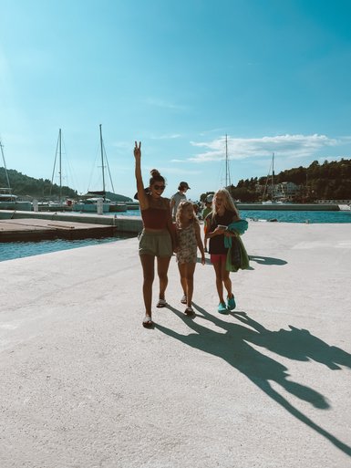 Eine fröhliche Familie spaziert am Hafen entlang, umgeben von Segelbooten und strahlend blauem Himmel.