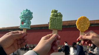 Drei Personen halten farbenfrohe Eis am Stiel in Form von chinesischen Symbolen vor einem historischen Hintergrund.