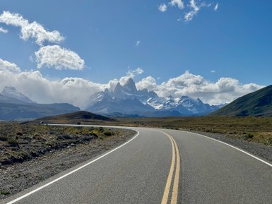Eine kurvenreiche Straße führt durch eine atemberaubende Landschaft mit schneebedeckten Bergen im Hintergrund.