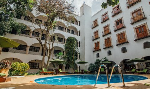 Ein einladender Innenhof mit einem blauen Pool, umgeben von üppigem Grün und gemütlichen Liegen unter Sonnenschirmen.