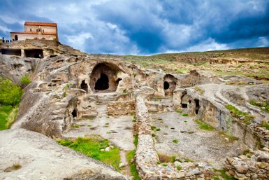 Die beeindruckenden Höhlen von Uplistsikhe sind in eine felsige Landschaft eingebettet, umgeben von sanften Hügeln und dramatischen Wolken.