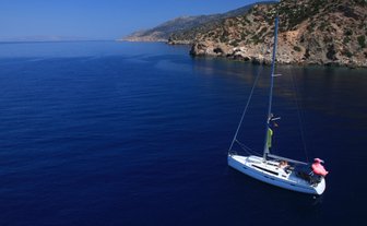 Ein Segelboot schaukelt sanft auf dem tiefblauen Wasser, umgeben von einer malerischen Küstenlandschaft.