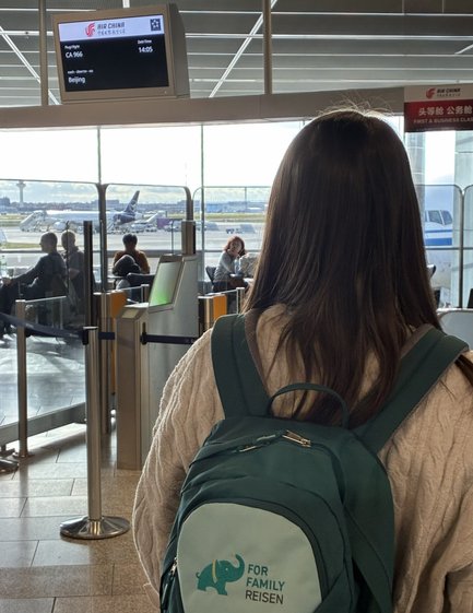 Eine Person mit einem grünen Rucksack steht am Flughafen und schaut auf die Anzeigetafel für Flüge nach Peking.