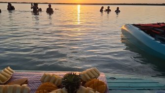 Eine Gruppe von Menschen schwimmt im ruhigen Wasser, während die Sonne am Horizont untergeht und den Himmel in warmen Farben färbt.