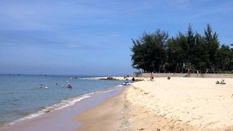 Ein sonniger Strand mit feinem Sand, wo Menschen im Wasser schwimmen und am Ufer entspannen.