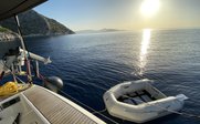 Ein ruhiger Morgen auf dem Wasser, mit einem kleinen Schlauchboot, das an einer Yacht festgemacht ist, und der Sonne, die aufgeht.