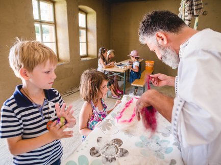 Ein älterer Mann zeigt Kindern, wie man mit buntem Filz arbeitet, während sie aufmerksam zuschauen und lernen.