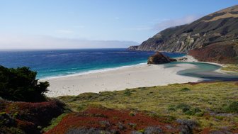 Ein atemberaubender Blick auf einen ruhigen Strand, umgeben von sanften Hügeln und klarem, blauem Wasser.
