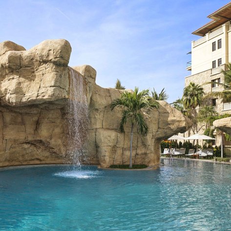 Ein luxuriöser Pool mit klarem Wasser, umgeben von Felsen und Palmen, bietet eine entspannende Atmosphäre.