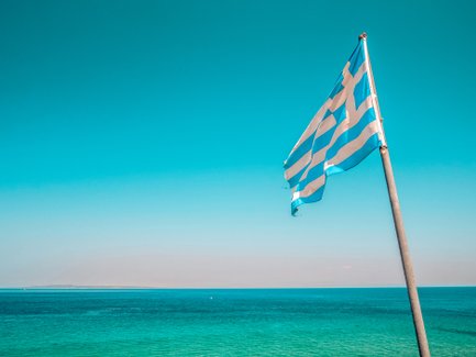Eine griechische Flagge weht sanft über dem klaren, blauen Wasser des Meeres unter einem strahlend blauen Himmel.