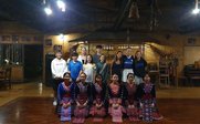 Eine Gruppe von Jugendlichen und Frauen in traditioneller Kleidung posiert in einem rustikalen Raum mit Holzdekor.