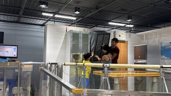 Eine Frau und ein Mann helfen einem Kind, einen großen Schrank während einer Erdbebensimulation zu stabilisieren.