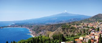 Ein atemberaubender Blick auf die Küste Siziliens, mit klarem blauen Wasser und üppigen grünen Hügeln im Vordergrund.