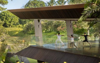 Drei Personen praktizieren Yoga auf einer überdachten Terrasse mit Blick auf eine grüne Landschaft in Bali.